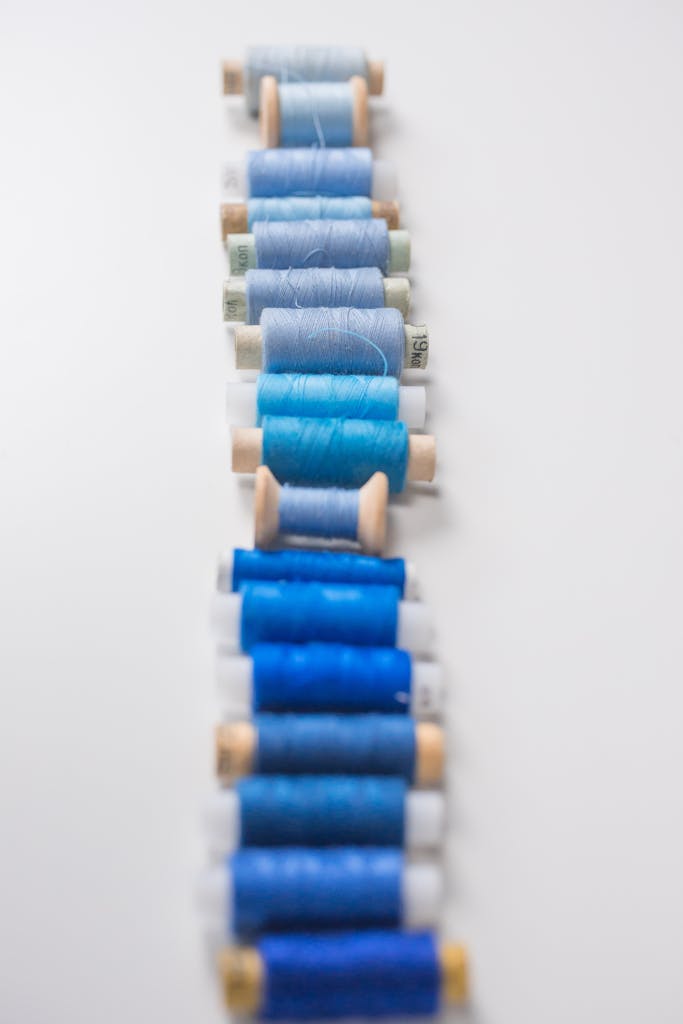 Blue sewing threads arranged in a vertical gradient on a white background. Perfect for craft or sewing projects.